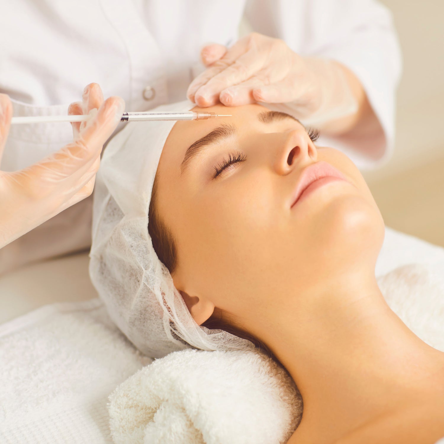 woman wearing white gloves putting dermal filler in someone's forehead